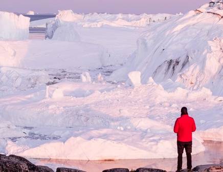 Man with a red coat hiking amongst the glaciers in Greenland