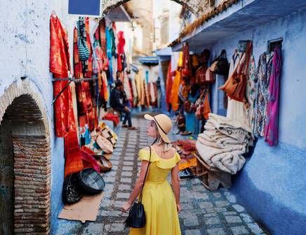 Une femme portant une robe jaune vif se promène dans les rues pittoresques et bleues de Chefchaouen