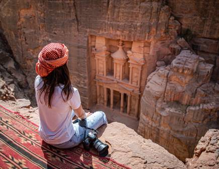 A woman wearing an orange turban gazing down at the Rose Red City of Petra, Jordan
