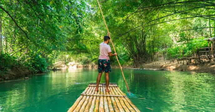 Ein Mann gleitet auf einem Bambusfloß durch grüne Gewässer