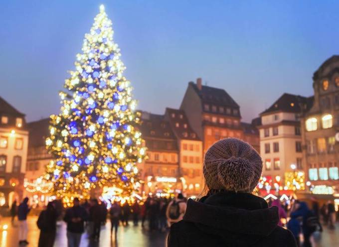 Une femme aux cheveux bruns portant un bonnet regarde un arbre de Noël sur un marché de Noël