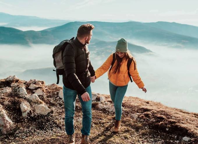 Un couple souriant et se tenant par la main alors qu'ils atteignent le sommet d'une montagne avec un