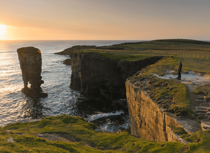 a man watches the sunset at the cliff