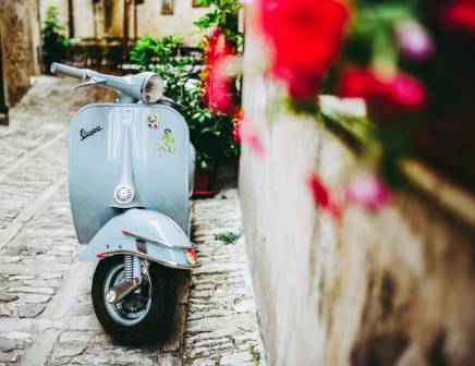 Light blue vespa parked on a narrow street in Italy.