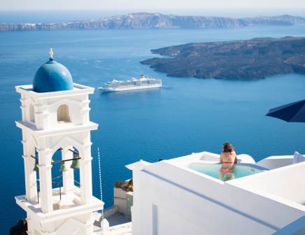 Woman relaxing in a swimming pool in Santorini observing the sea.