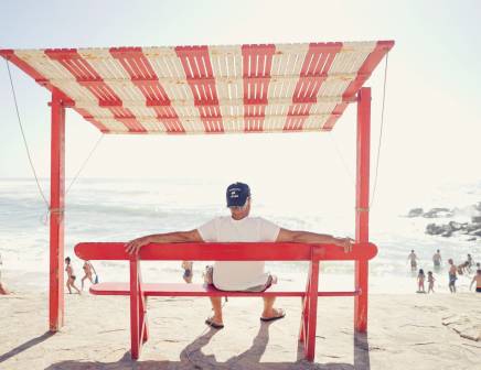 Older man sitting alone on a red bench observing the sea.