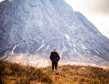 Man standing alone in a meadow admiring Scottish Highlands.