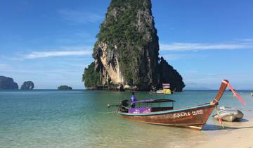 Traditional longtail boat on a tropical beach with clear water and limestone cliffs.