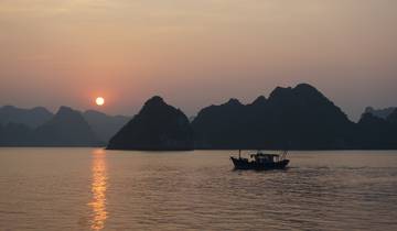 Boat sailing at sunset with limestone mountains in the background.