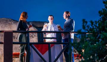 Three people on a deck enjoying drinks with thatched roofs in the background.