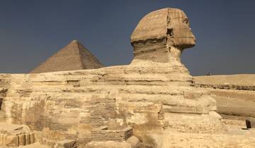 The Sphinx with a backdrop of a pyramid in the desert.