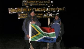 Two people holding a flag at Uhuru Peak, Mount Kilimanjaro at night