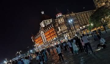 Crowded square with people and a lit historical building at night.