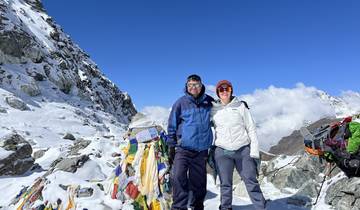 Hikers at the summit of a snow-capped mountain with prayer flags.