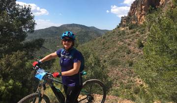 Woman with a bicycle, posing outdoors with mountains in the background.
