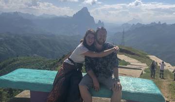 Two people sitting on a bench with a mountainous view in the background.
