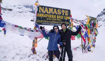 Two people at Annapurna Base Camp with snow and prayer flags.