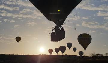 Hot air balloons rising at sunrise in a rocky landscape.