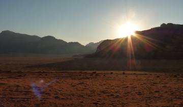 Desert landscape with sun setting behind mountains.