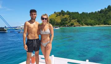Couple standing on a boat with turquoise waters and lush islands.