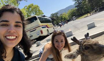 Two people posing with a deer in an open area with trees.