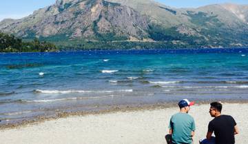 Two people sitting by a lake with mountains in the background.