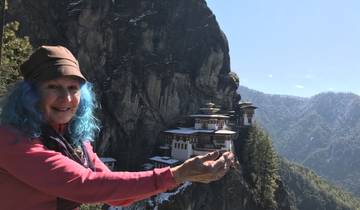 Person posing with hands open towards Taktsang (Tiger's Nest) Monastery on a cliff.