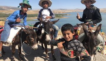 Children riding donkeys with a scenic background of a water body.