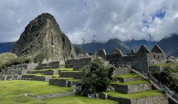 Ruins with mountainous backdrop and cloudy sky.