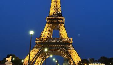 Illuminated Eiffel Tower at night with visitors.