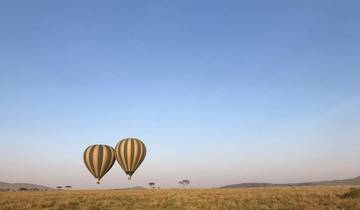 Two hot air balloons floating over a vast open savanna.
