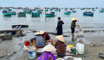 People sorting fish on a beach, boats in the background.