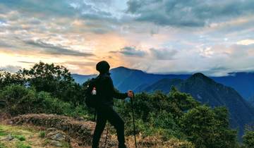 Person standing with hiking poles looking at view of mountains at sunset.