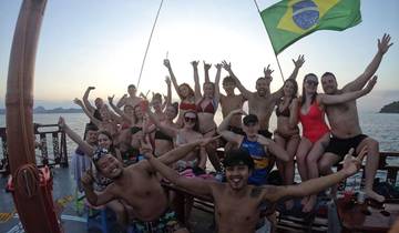 Group of people celebrating on a boat with a Brazilian flag at sunset.