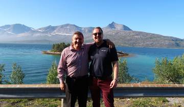 Two people posing by a scenic lake with mountains.