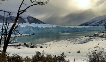 Scenic view of a massive glacier meeting a lake with mountains in the background.
