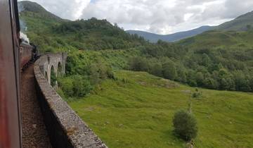 A train crossing a scenic viaduct among green hills.