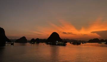 Boats in Halong Bay at sunset with silhouette islands.