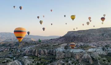 Hot air balloons rising over Cappadocia landscape.