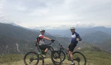 Two cyclists at a mountain peak with a vast landscape.