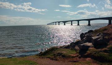 Long bridge over shimmering water with rocky shore.