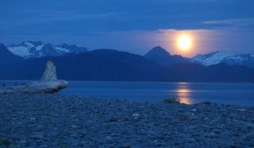Moon setting over a calm sea with mountain range.