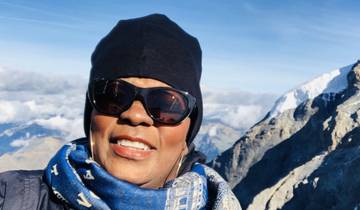 Person posing with sunglasses against a mountain background.
