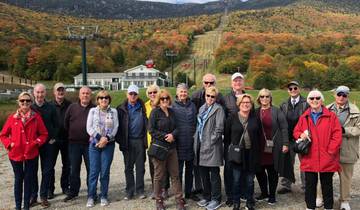A group of people posing in front of a scenic mountain landscape in autumn.