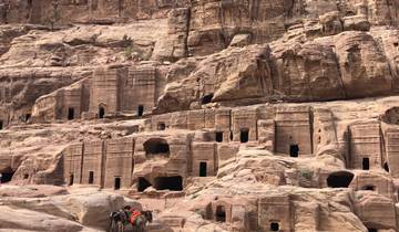 Ancient rock-cut tombs in Petra, people and camels in the foreground.