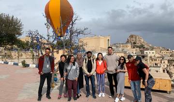 Group of people posing with a hot air balloon sculpture in a Turkish village setting with a castle in the background.