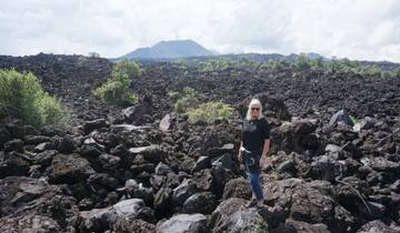 Woman standing on volcanic rocks with a volcano in the background.