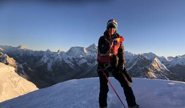 Hiker on a snowy peak with a view of other mountain ranges.