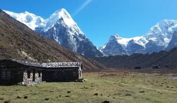 Small stone house in a valley surrounded by snow-capped mountains.