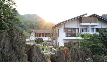 Sun setting behind a house with mountains in the background.